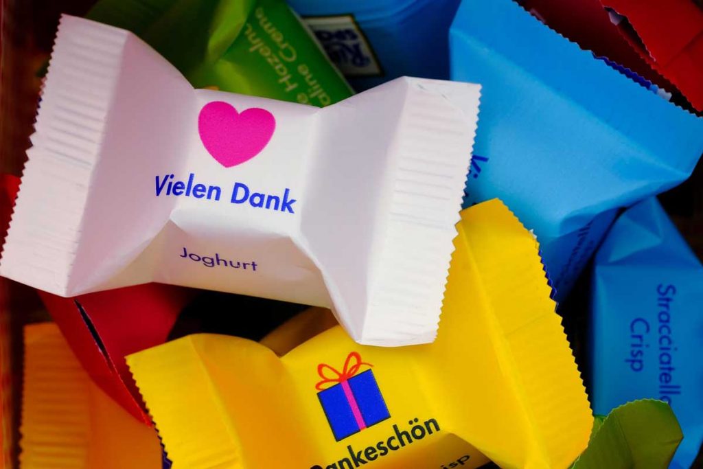 Kundenfeedback: Worte, die uns besonders freuen - P.S.I. Speditions GmbH Symbolbild für ein Dankeschön für ein tolles Kundenfeedback: Kleine, einzeln verpackte Schokowürfel mit Danke-Aufschriften und Herz- und Geschenk-Piktogrammen